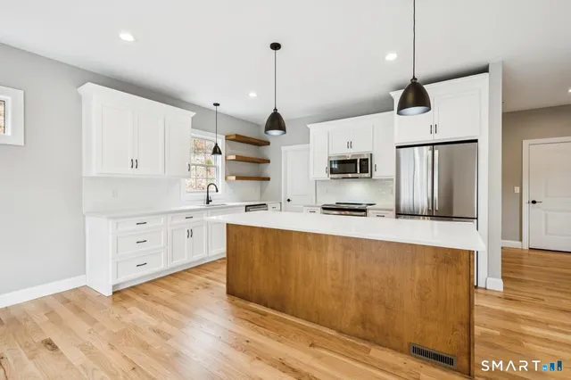 a large kitchen with white cabinets stainless steel appliances and wooden floor