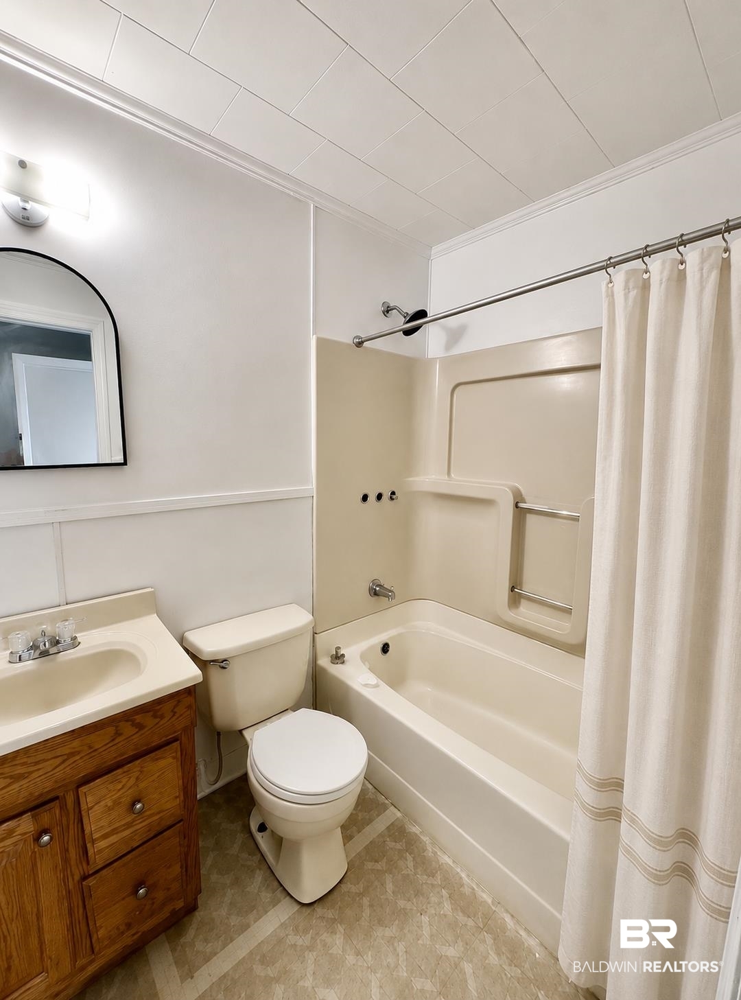 226 Elizabeth Street Evergreen, AL 36401 - Photo 26 of 35 Bathroom featuring a built-in tub and shower combination with a curved shower rod, a wood-finish vanity with an integrated sink, a toilet, and a wall-mounted arched mirror