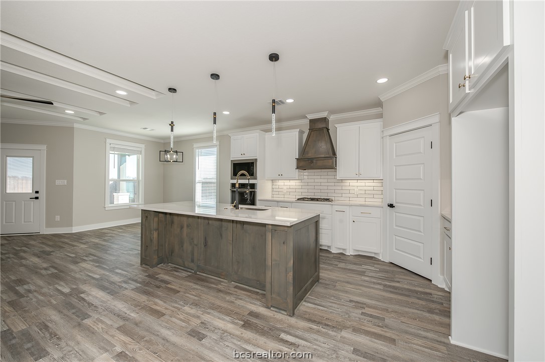 2908 GOLDBERG Drive Bryan, TX 77808 - Photo 23 of 44 Modern kitchen features: stainless steel appliances, quartz countertops, stained island, painted cabinets, decorative pendant lights, cabinet hardware, vinyl flooring, and tile backsplash.