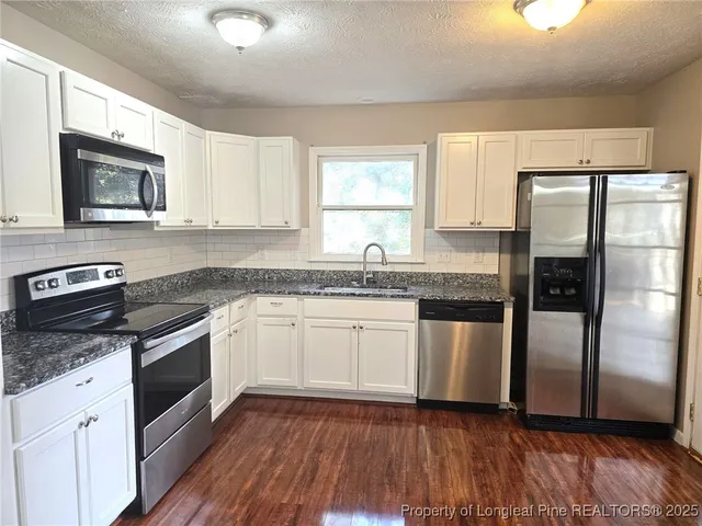 a kitchen with granite countertop wooden floors appliances and sink