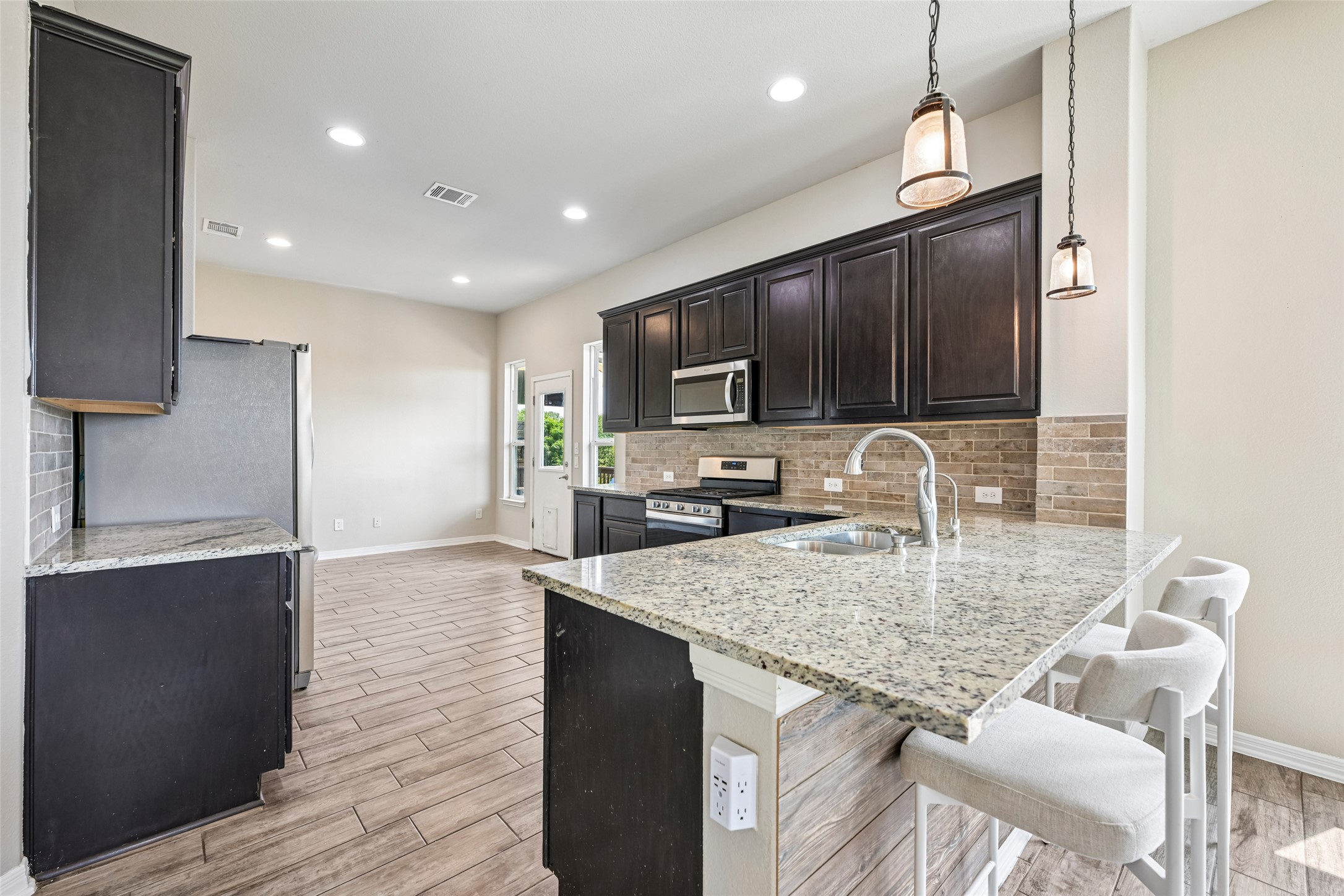 1297 Harwell Loop Kyle, TX 78640 - Photo 15 of 39 Granite counters and dark cabinetry create a sleek, contemporary kitchen space with an inviting breakfast bar.