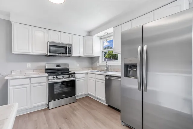 a kitchen with kitchen island granite countertop a stove top oven a sink and dishwasher a refrigerator with white cabinets