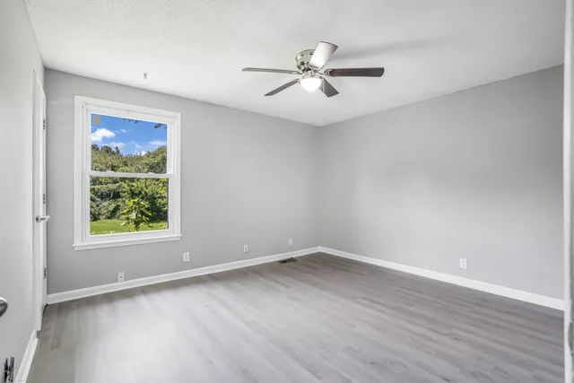 an empty room with wooden floor chandelier fan and windows