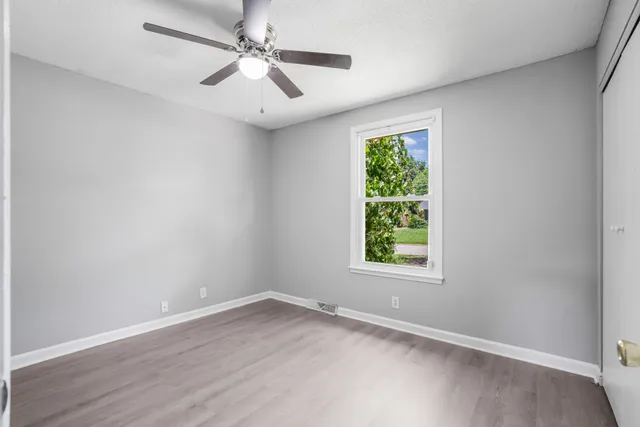 an empty room with wooden floor ceiling fan and windows