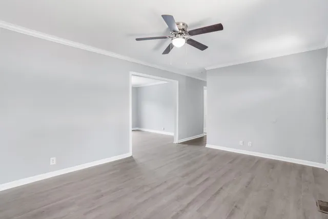 a view of an empty room with wooden floor and a ceiling fan