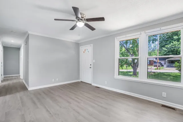 an empty room with wooden floor fan and windows