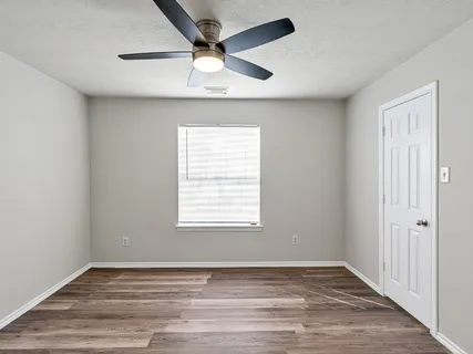 an empty room with wooden floor fan and windows