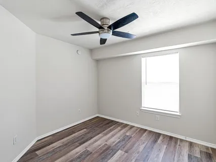 an empty room with wooden floor ceiling fan and windows