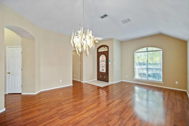 an empty room with wooden floor chandelier and windows