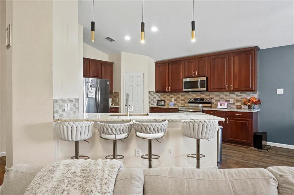 1412 Cheyenne Road Wylie, TX 75098 - Photo 11 of 24 Kitchen with a kitchen breakfast bar, tasteful backsplash, light stone counters, vaulted ceiling, and dark wood-style flooring