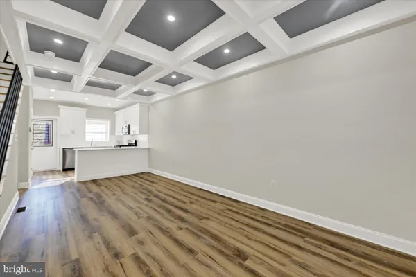 a view of empty room with wooden floor and kitchen view