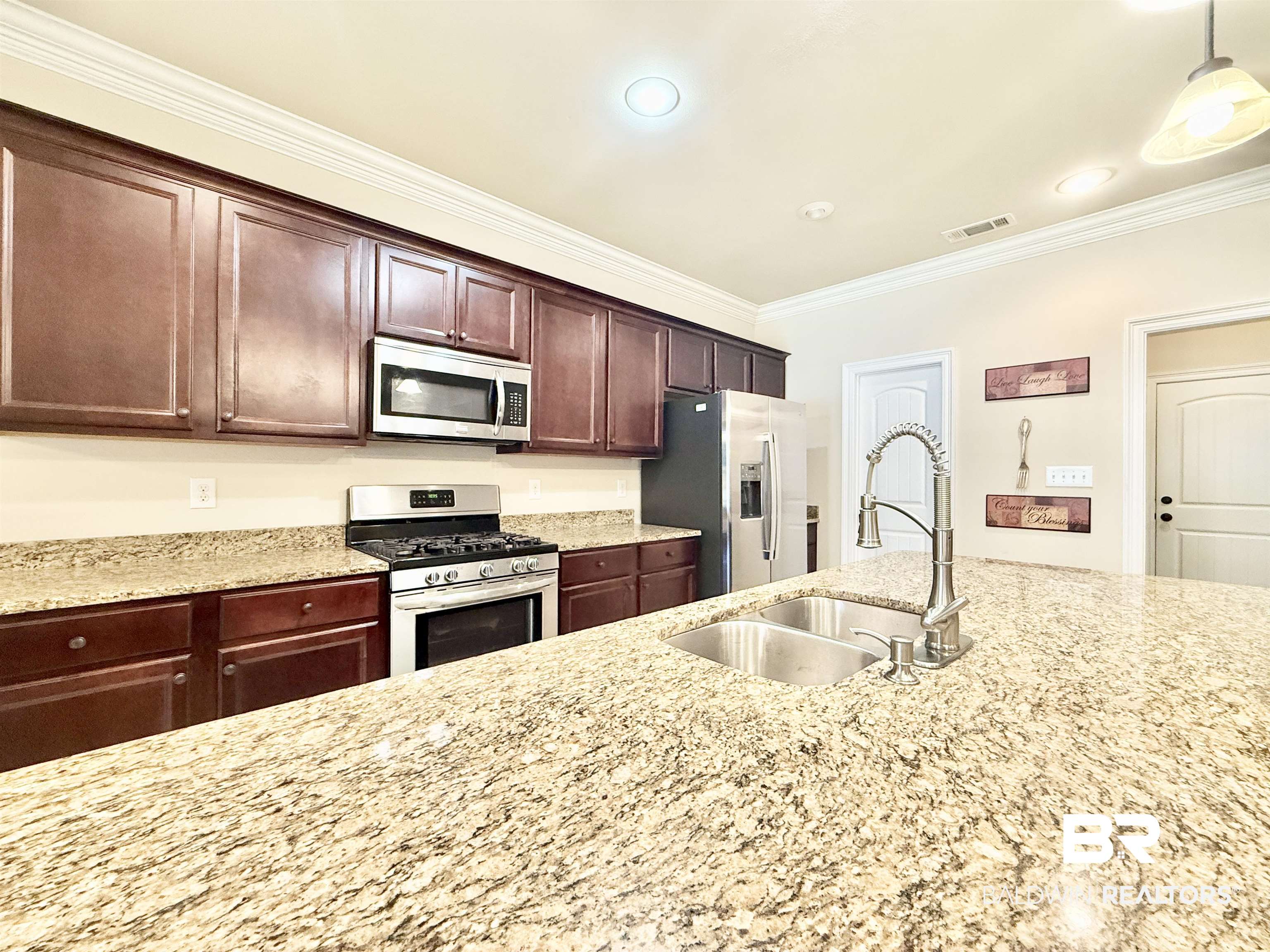 7011 Rocky Rd Loop Gulf Shores, AL 36542 - Photo 13 of 66 Kitchen featuring ornamental molding, stainless steel appliances, dark brown cabinetry, light stone counters, and pendant lighting