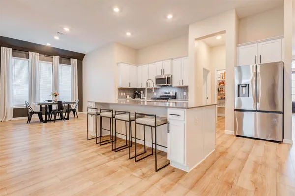 a kitchen with stainless steel appliances a refrigerator a stove a sink a dining table and chairs with wooden floor