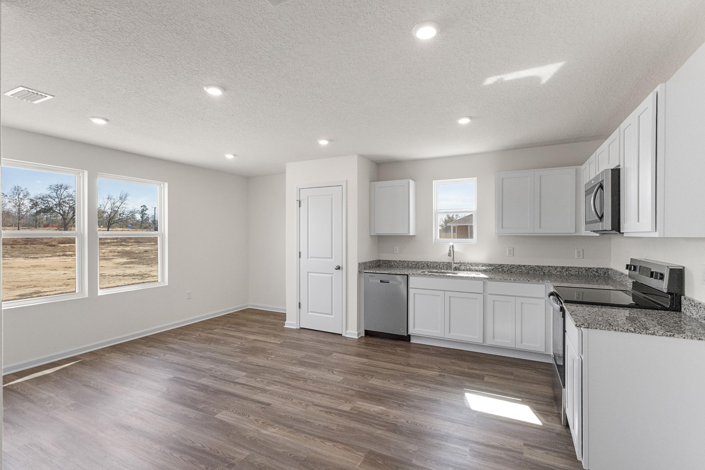 291 Cat Island Road DeFuniak Springs, FL 32433 - Photo 6 of 18 a large kitchen with granite countertop a stove a sink a refrigerator and white cabinets with wooden floor