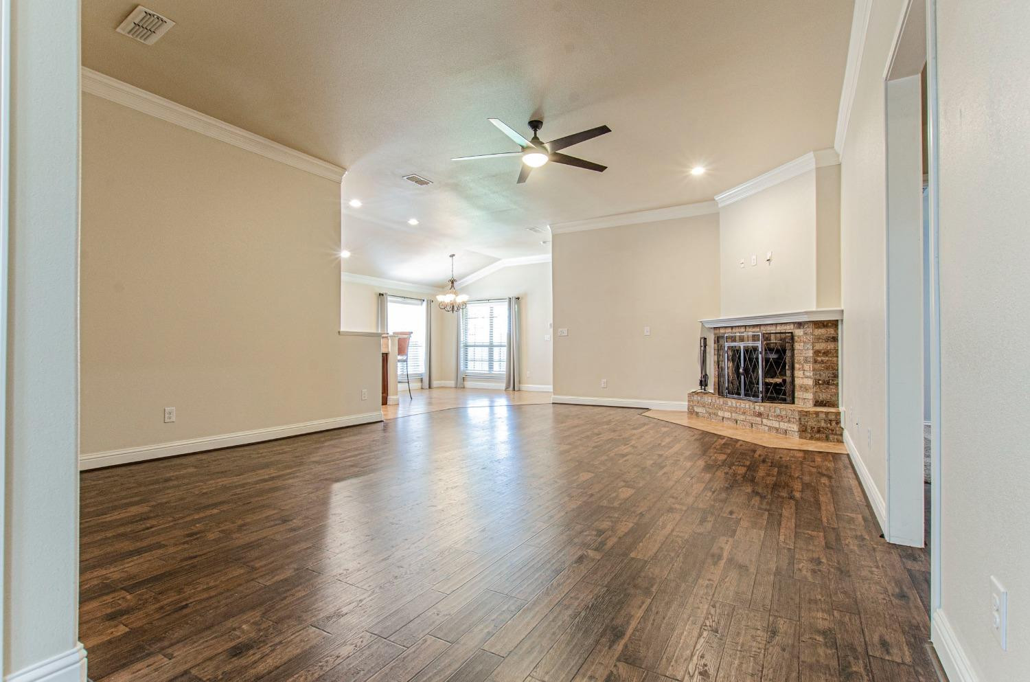 9105 Rochester Avenue Lubbock, TX 79424 - Photo 20 of 24 an empty room with wooden floor a ceiling fan and kitchen view