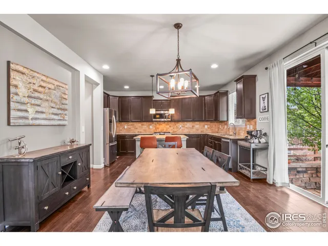 a kitchen with stainless steel appliances kitchen island granite countertop a stove a refrigerator a sink a dining table and chairs with wooden floor