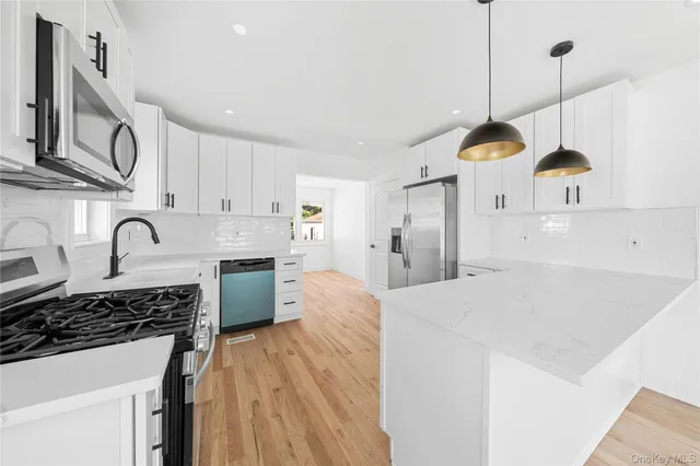 a large kitchen with stainless steel appliances granite countertop a stove a sink a refrigerator and white cabinets with wooden floor