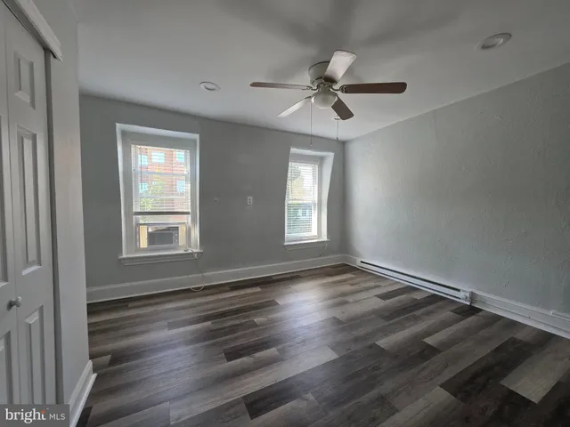 an empty room with wooden floor fan and windows