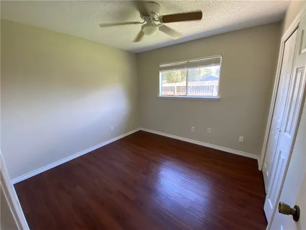 an empty room with wooden floor fan and windows