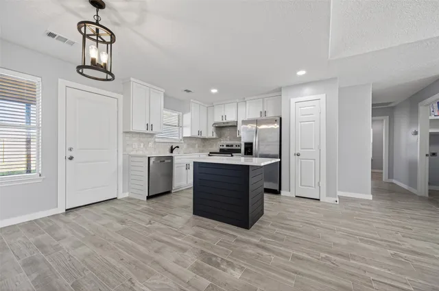 a kitchen with stainless steel appliances granite countertop a refrigerator a sink dishwasher a stove and white countertops with wooden floor