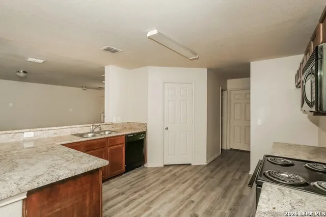 a view of empty room with wooden floor and kitchen