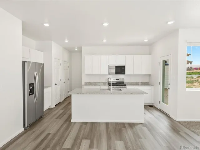 a large white kitchen with kitchen island a sink dishwasher a refrigerator and a stove with wooden floor