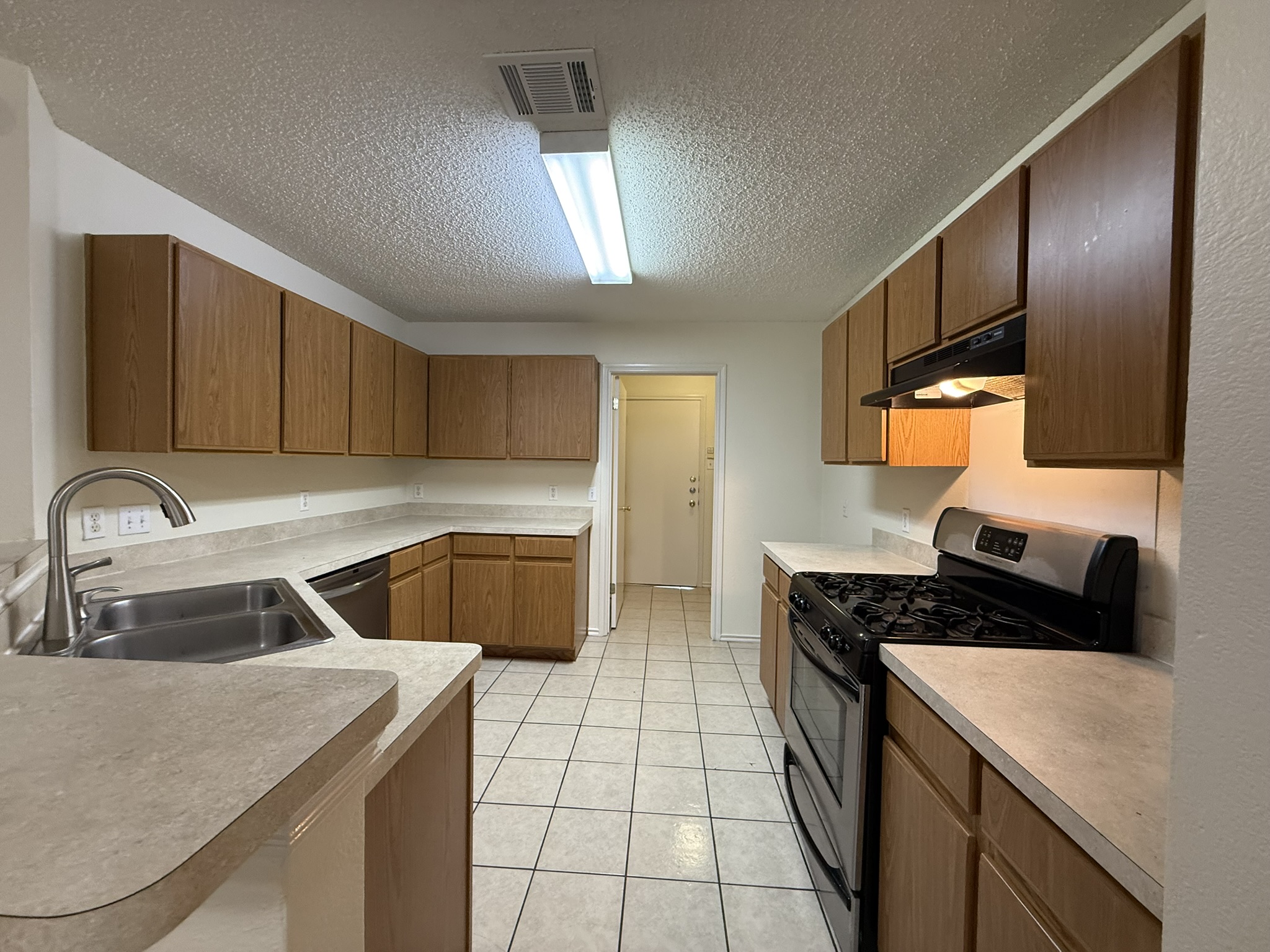 2304 Granberry Drive, Unit B Austin, TX 78745 - Photo 11 of 24 Kitchen featuring wood-finish cabinetry, light-toned countertops, a stainless steel double basin sink with a high-arch faucet, a black gas range with a stainless steel control panel, and tile flooring