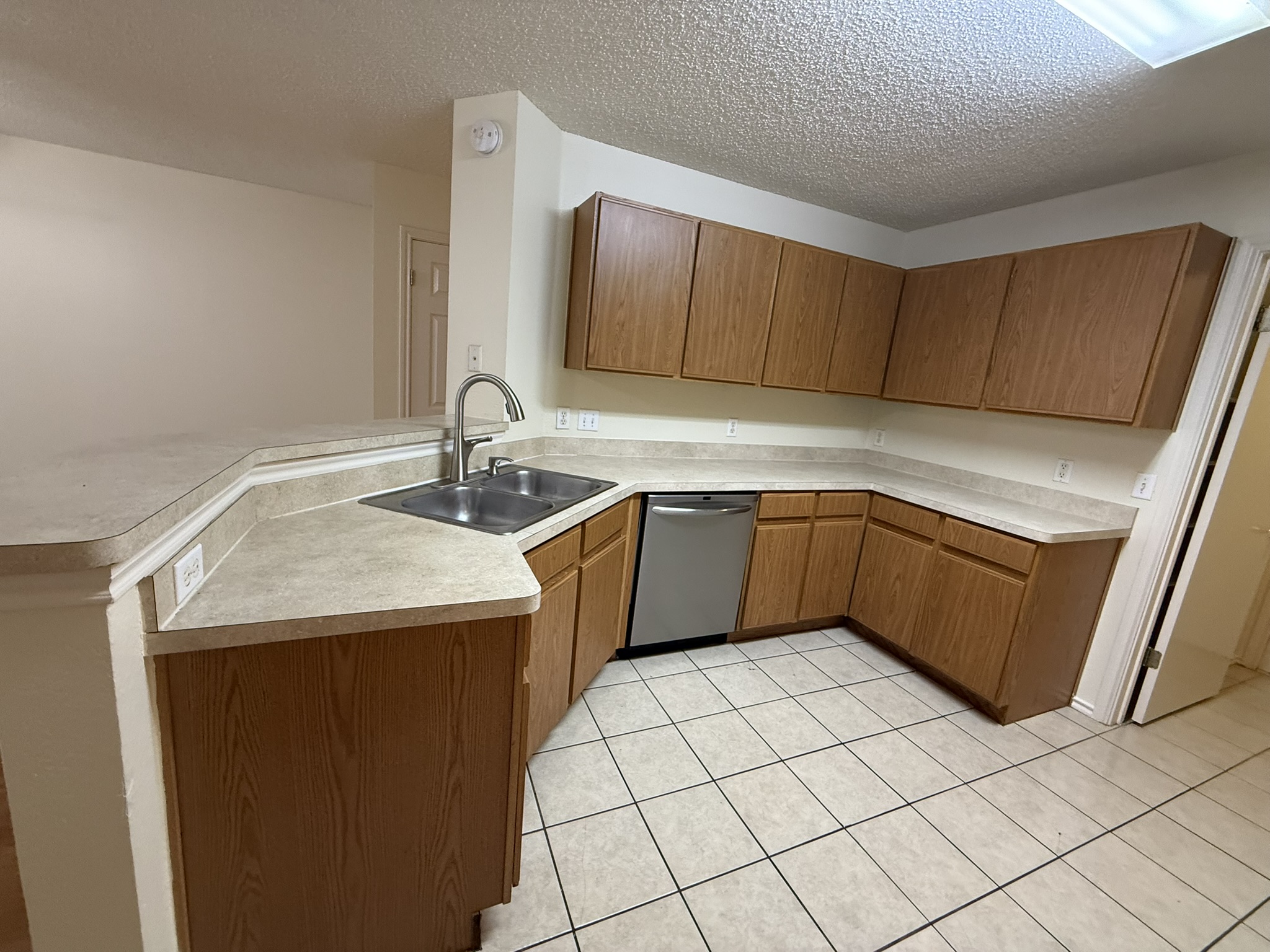 2304 Granberry Drive, Unit B Austin, TX 78745 - Photo 12 of 24 Kitchen featuring a stainless steel double basin sink with a high-arch faucet, wood-finish cabinetry, light-toned laminate countertops, and tile flooring