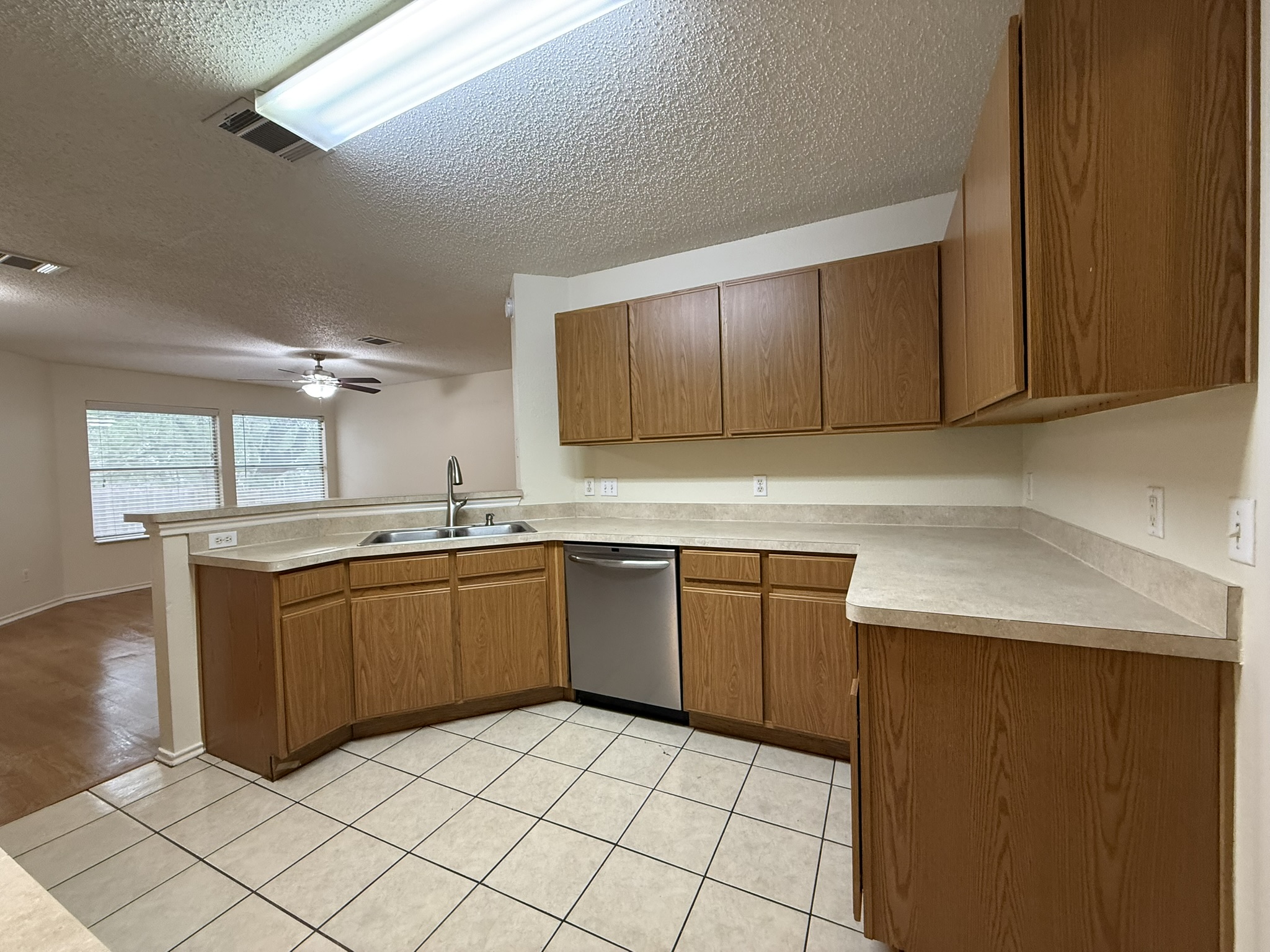 2304 Granberry Drive, Unit B Austin, TX 78745 - Photo 13 of 24 U-shaped kitchen featuring wood-finish cabinetry, a stainless steel dishwasher, and an integrated sink with a chrome faucet