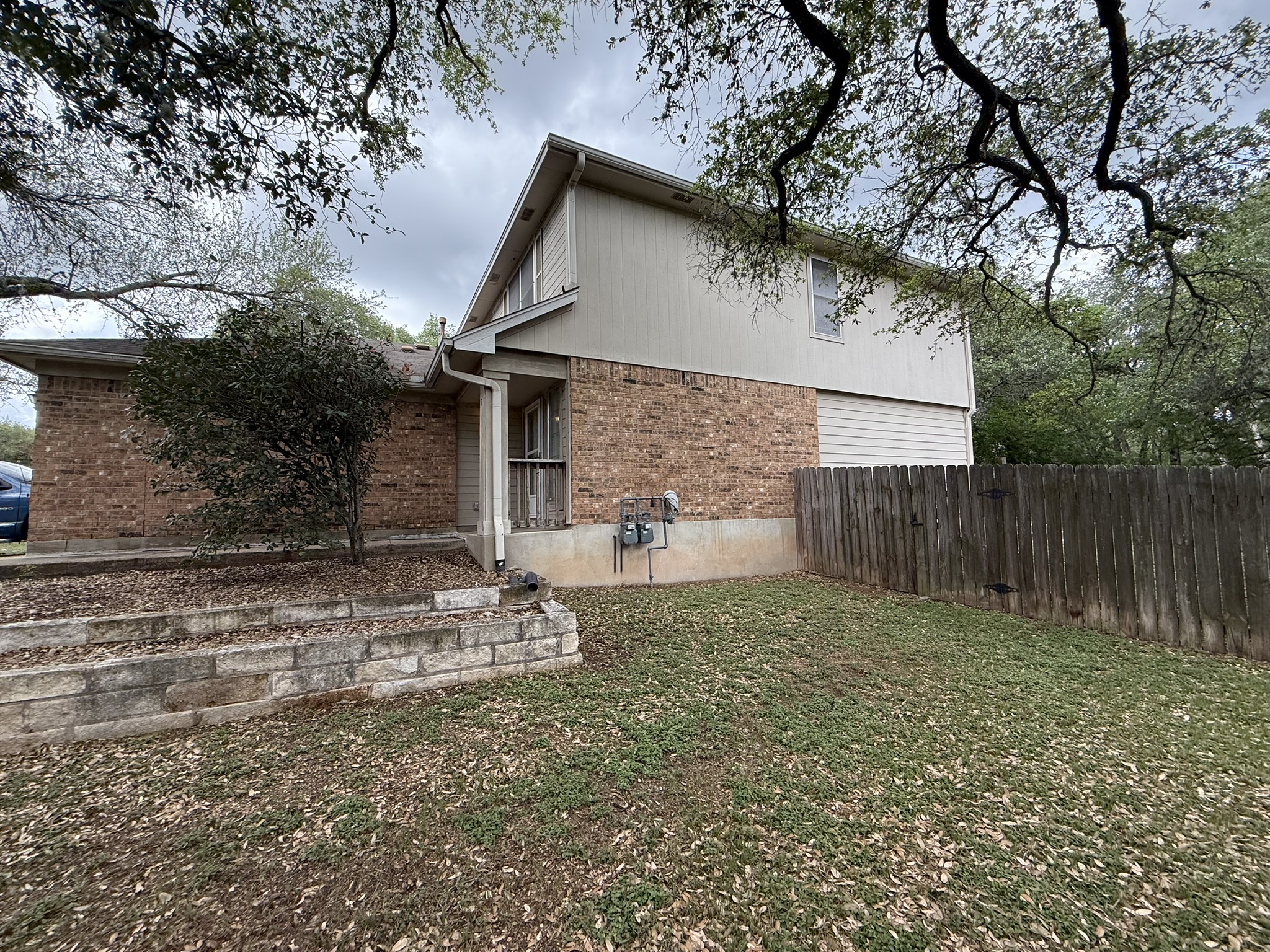 2304 Granberry Drive, Unit B Austin, TX 78745 - Photo 2 of 24 Exterior featuring brick and vertical siding, a tiered stone retaining wall, mature perimeter trees, and a wooden privacy fence