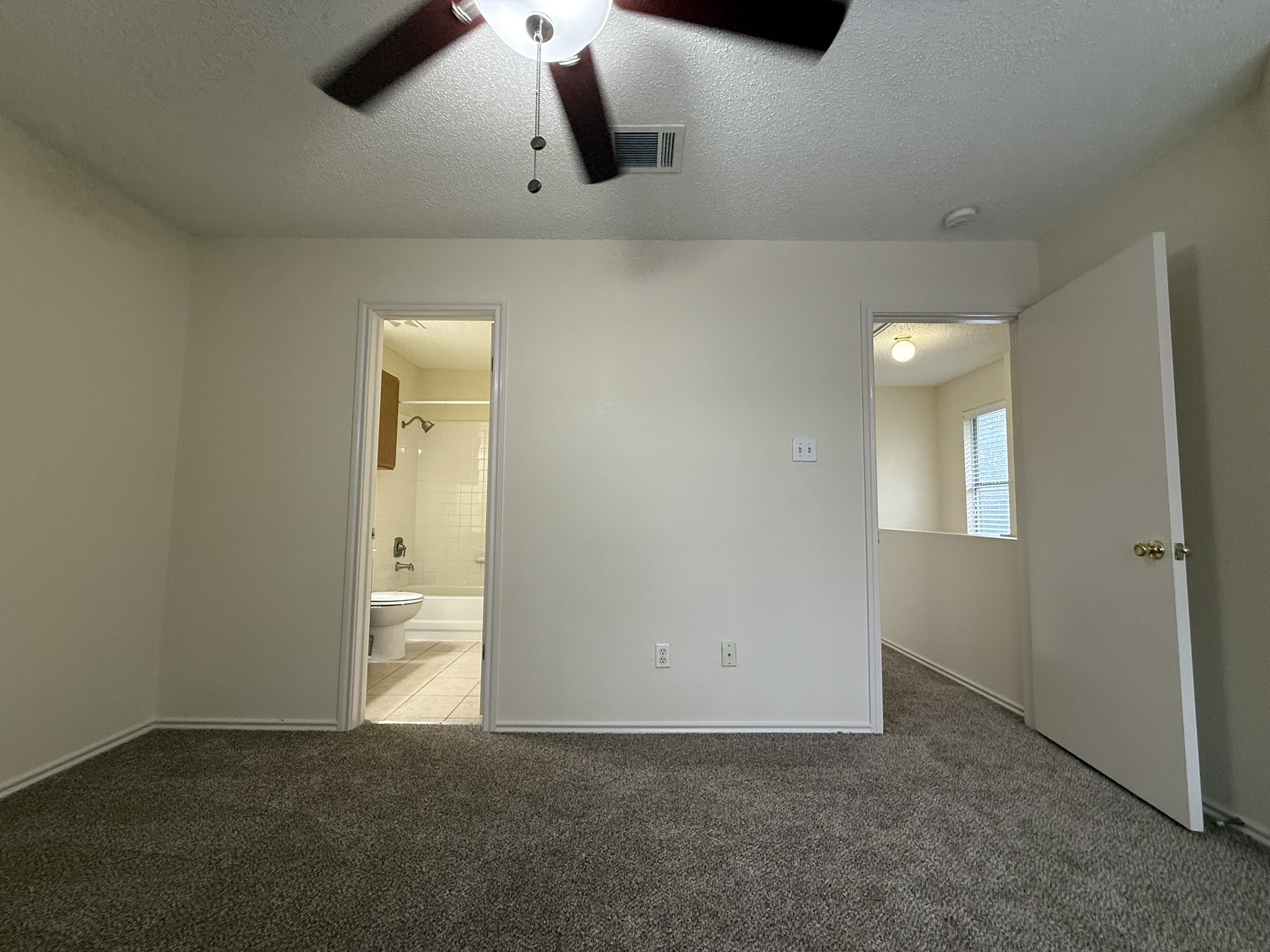 2304 Granberry Drive, Unit B Austin, TX 78745 - Photo 23 of 24 Carpeted room with a ceiling fan light fixture, featuring a doorway opening to a bathroom with a tiled floor, white tub/shower combination, and toilet