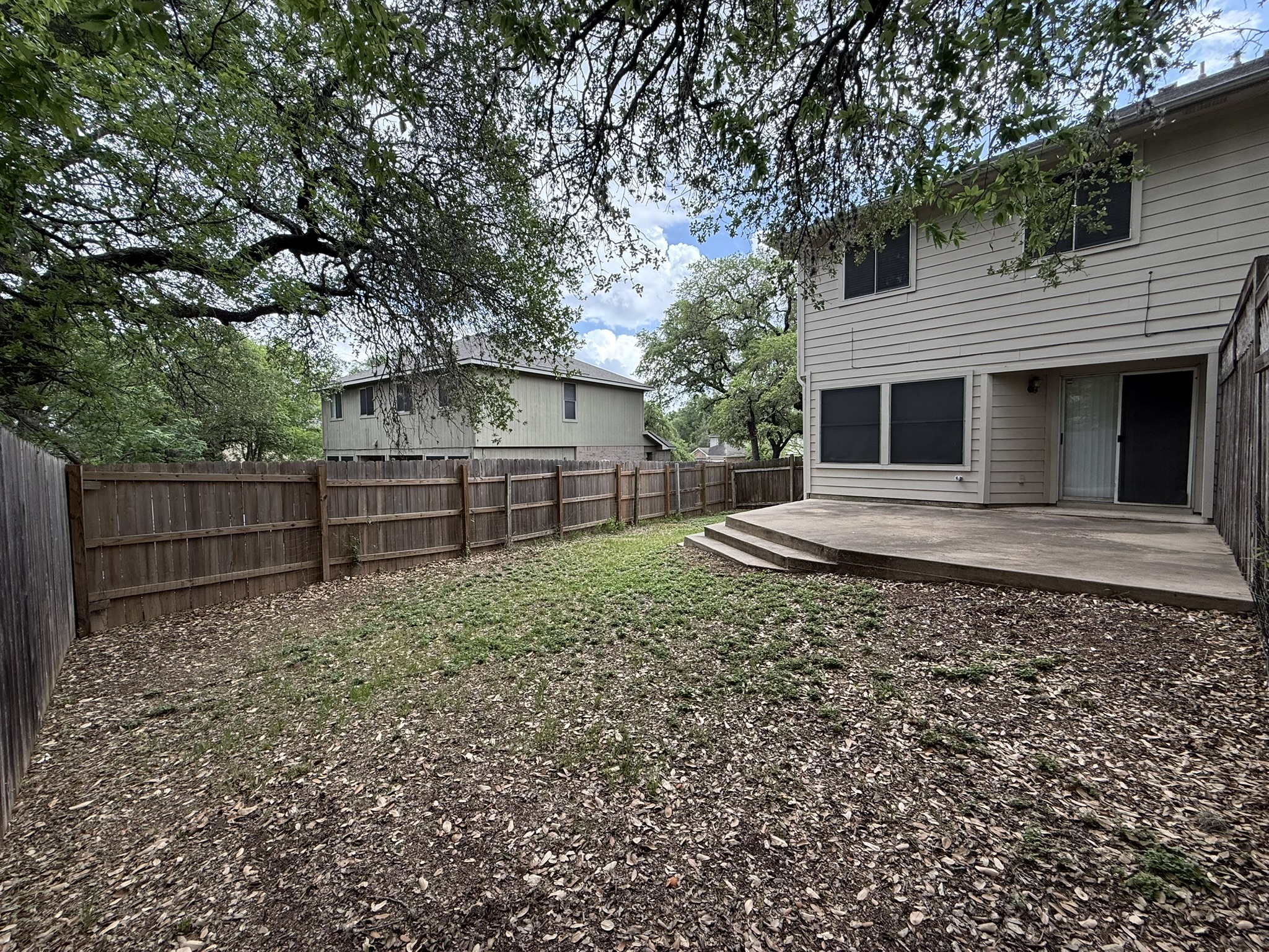 2304 Granberry Drive, Unit B Austin, TX 78745 - Photo 4 of 24 Expansive backyard featuring a concrete patio with steps, a full wood privacy fence, and mature trees providing natural shade