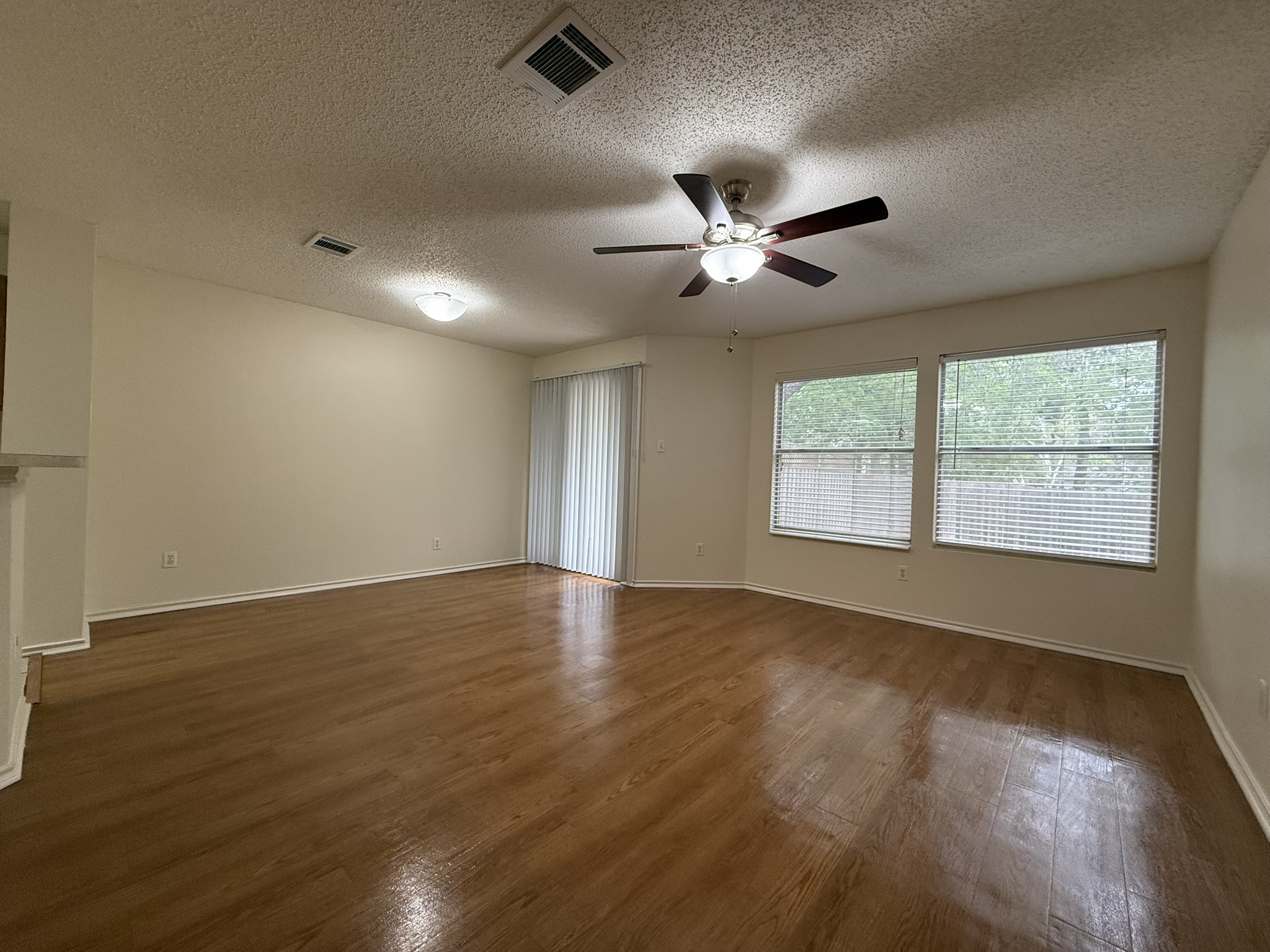2304 Granberry Drive, Unit B Austin, TX 78745 - Photo 6 of 24 Spacious living area featuring wood-finish flooring, a ceiling fan with integrated lighting, multiple windows with blinds, and a sliding glass door