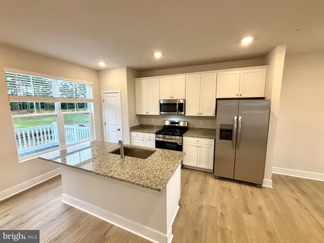 a kitchen with granite countertop a stove a sink a refrigerator a window and cabinets