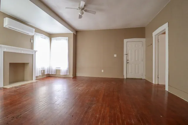 an empty room with wooden floor fireplace and windows