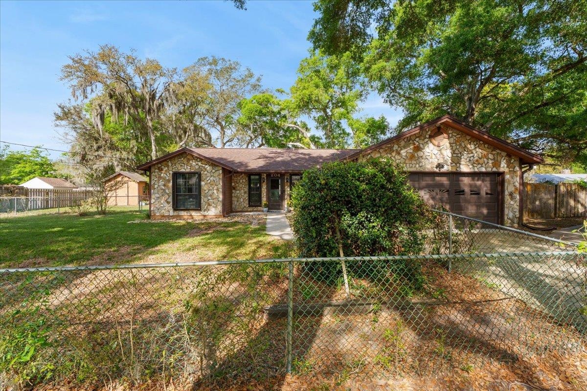 204 Queen Road St. Augustine, FL 32086 - Photo 2 of 55 View of front facade featuring stone siding, a fenced front yard, a garage, and driveway