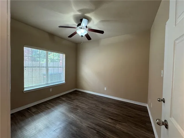 an empty room with wooden floor chandelier fan and windows