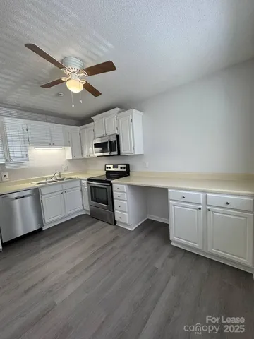 a kitchen with stainless steel appliances white cabinets a sink a stove a microwave and wooden floors