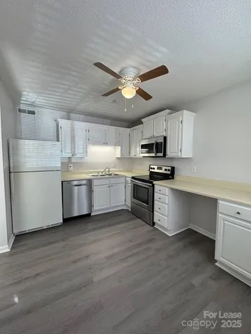 a kitchen with granite countertop a refrigerator a sink dishwasher and a stove top oven with white cabinets