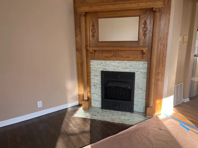 a view of an empty room with wooden floor and a fireplace