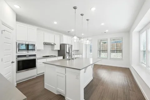 a kitchen with stainless steel appliances granite countertop a sink a stove a refrigerator cabinets and a wooden floor