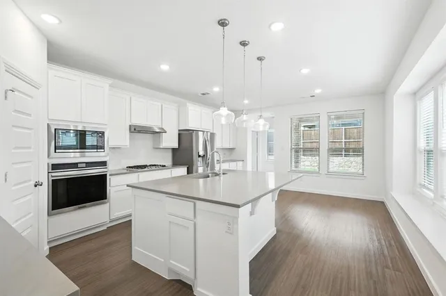 a kitchen with stainless steel appliances granite countertop a sink a stove a refrigerator cabinets and a wooden floor