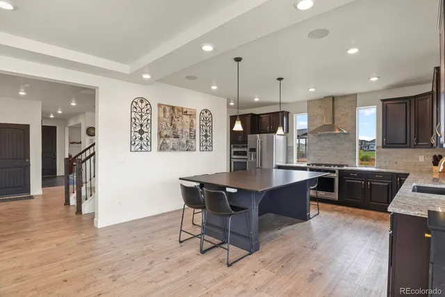 a kitchen with stainless steel appliances kitchen island granite countertop a refrigerator a stove a sink a dining table and chairs with wooden floor