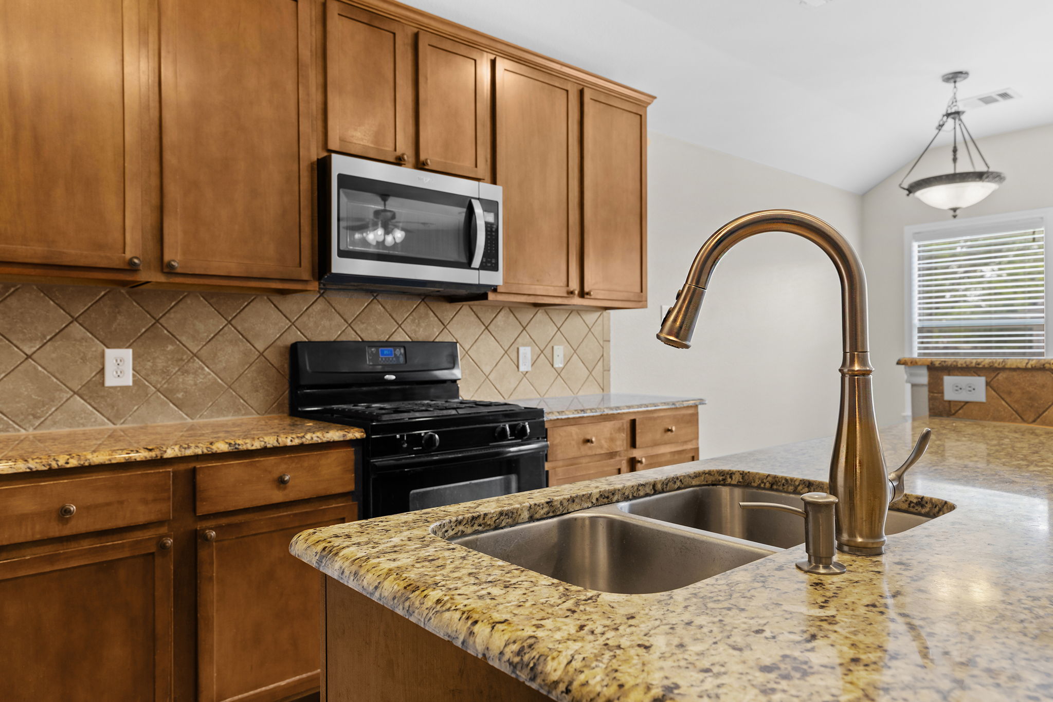 3013 Hawks Swoop Trail Pflugerville, TX 78660 - Photo 13 of 40 Kitchen with black gas range oven, stainless steel microwave, light stone countertops, backsplash, and lofted ceiling