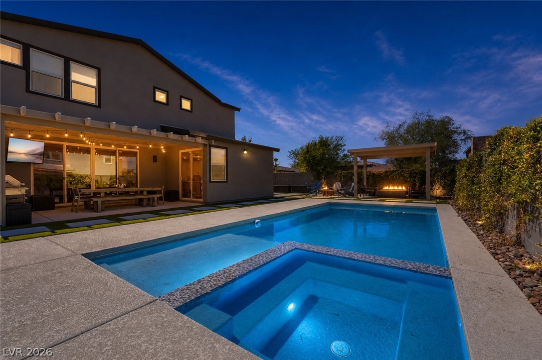 2166 Trivero Street Henderson, NV 89044 - Photo 53 of 61 A spacious backyard retreat features an illuminated pool and spa, alongside an outdoor patio area and fire pit.