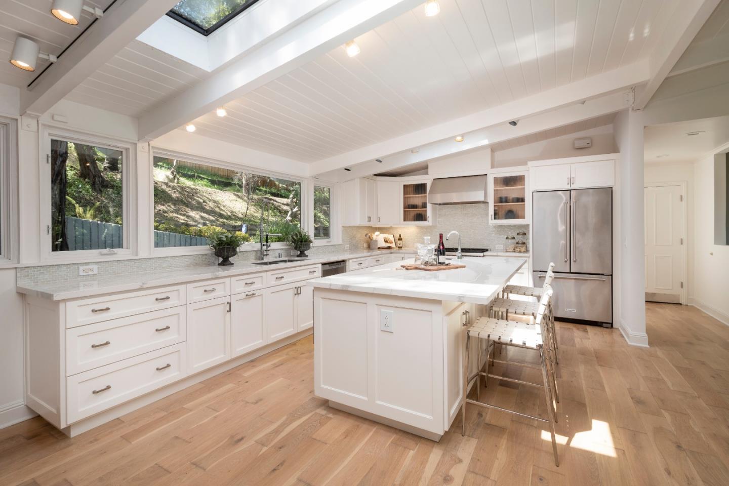 a kitchen with stainless steel appliances kitchen island granite countertop a stove a sink a refrigerator and white cabinets with wooden floor