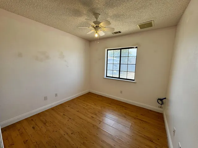 an empty room with wooden floor chandelier fan and windows