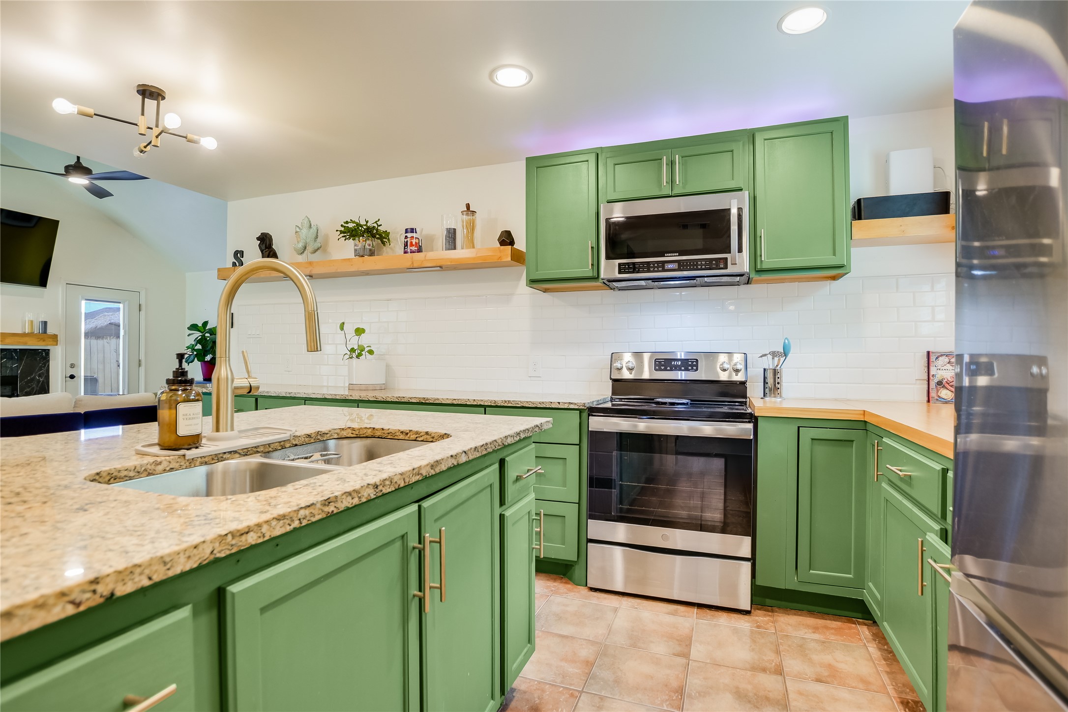 4702 Crest Oak Road Austin, TX 78744 - Photo 8 of 20 Kitchen featuring green cabinetry, granite countertops, stainless steel appliances, subway tile backsplash, and a gold-finish faucet