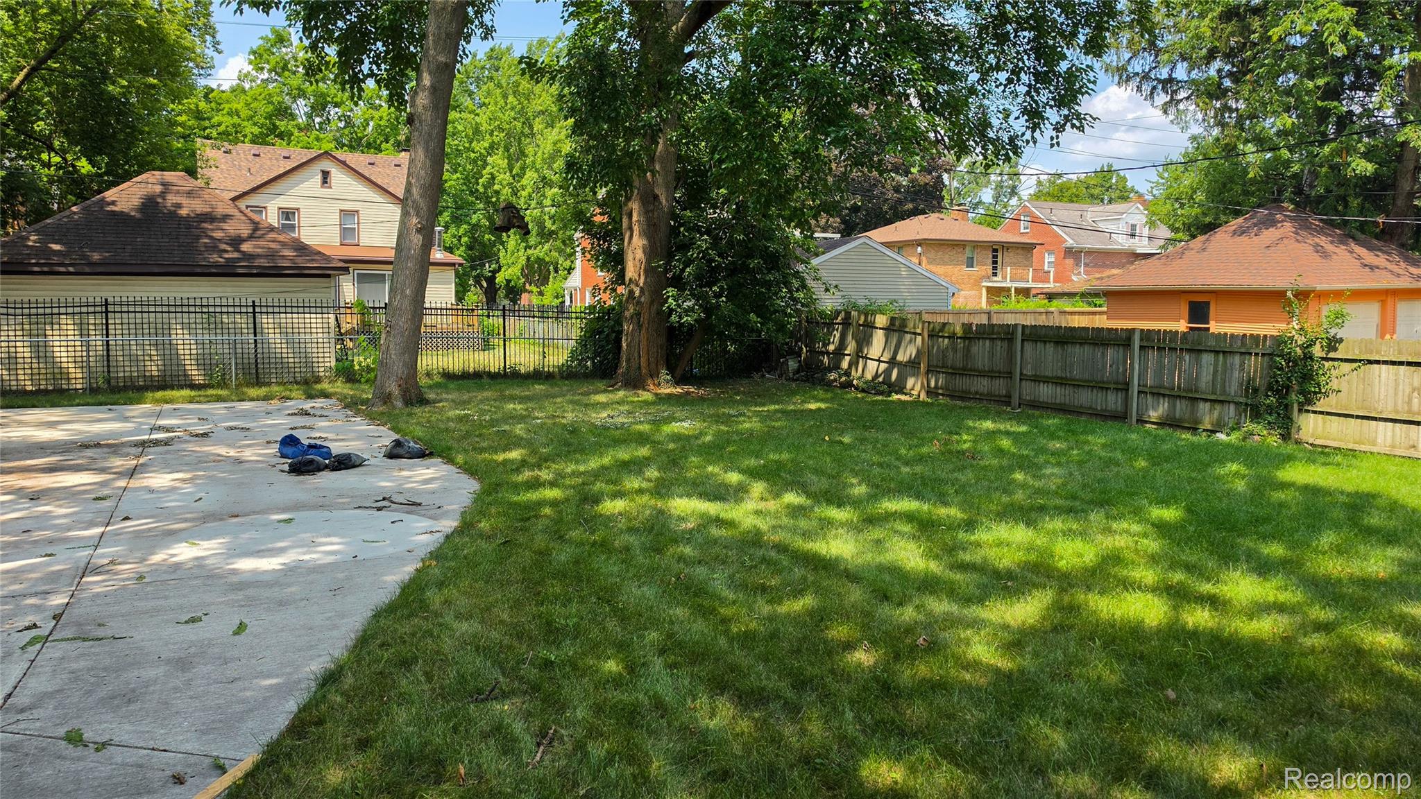 16715 Edinborough Road Detroit, MI 48219 - Photo 20 of 21 Expansive rear yard featuring a concrete patio, established trees, and a wooden privacy fence