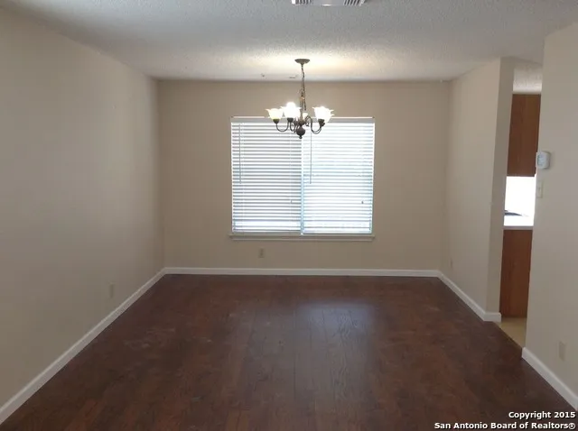 an empty room with wooden floor chandelier and windows
